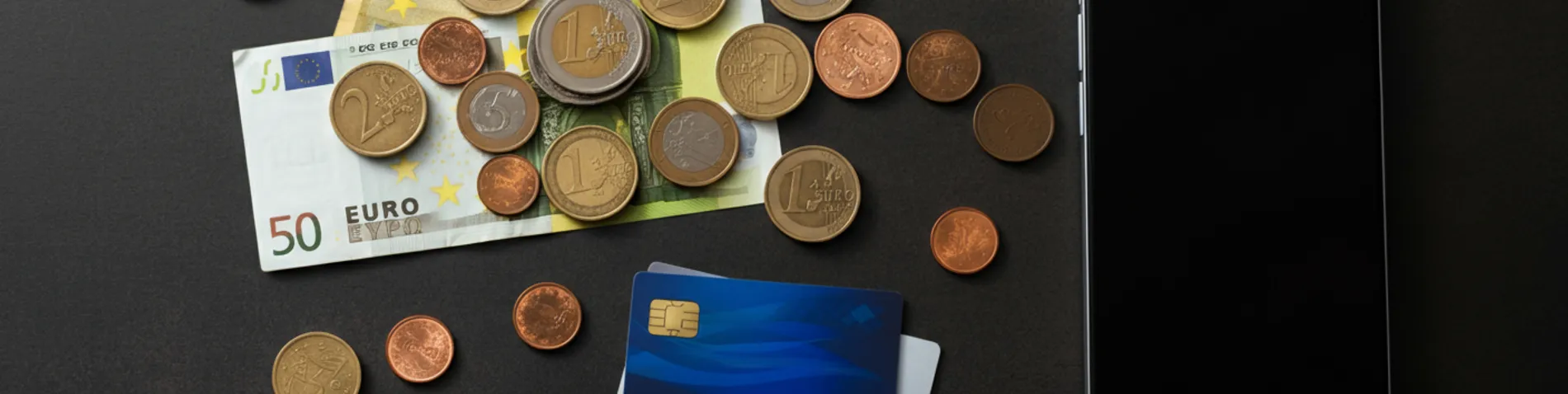 Billetes y monedas de euro junto a tarjetas de crédito y smartphone sobre superficie oscura