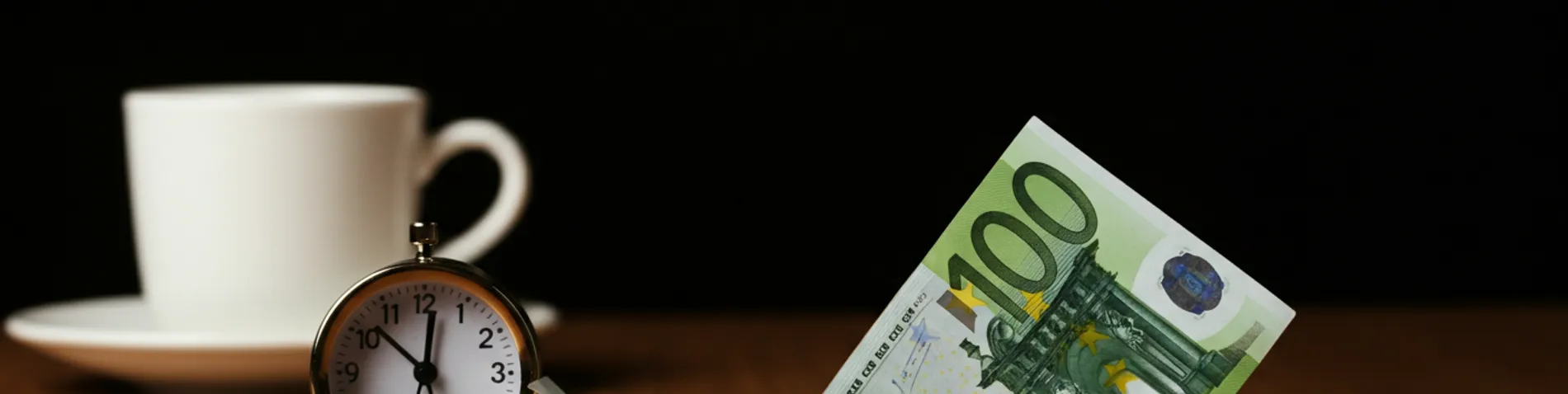 Billete de euro encogiendo poco a poco sobre una mesa junto a un reloj y una taza de café